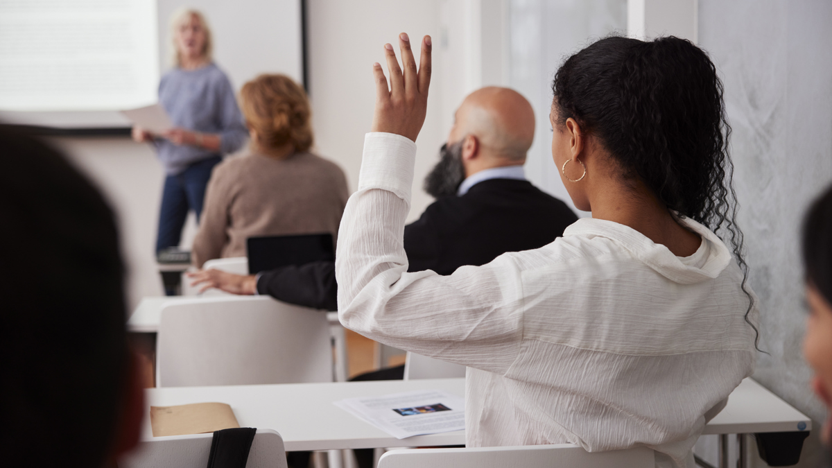 Kvinna i klassrum håller upp handen.