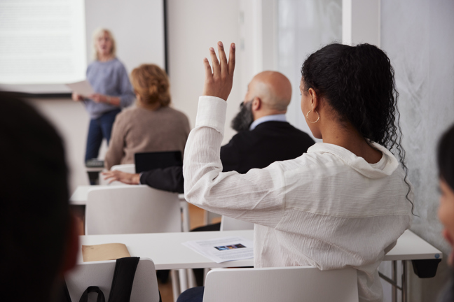 Kvinna i klassrum håller upp handen.